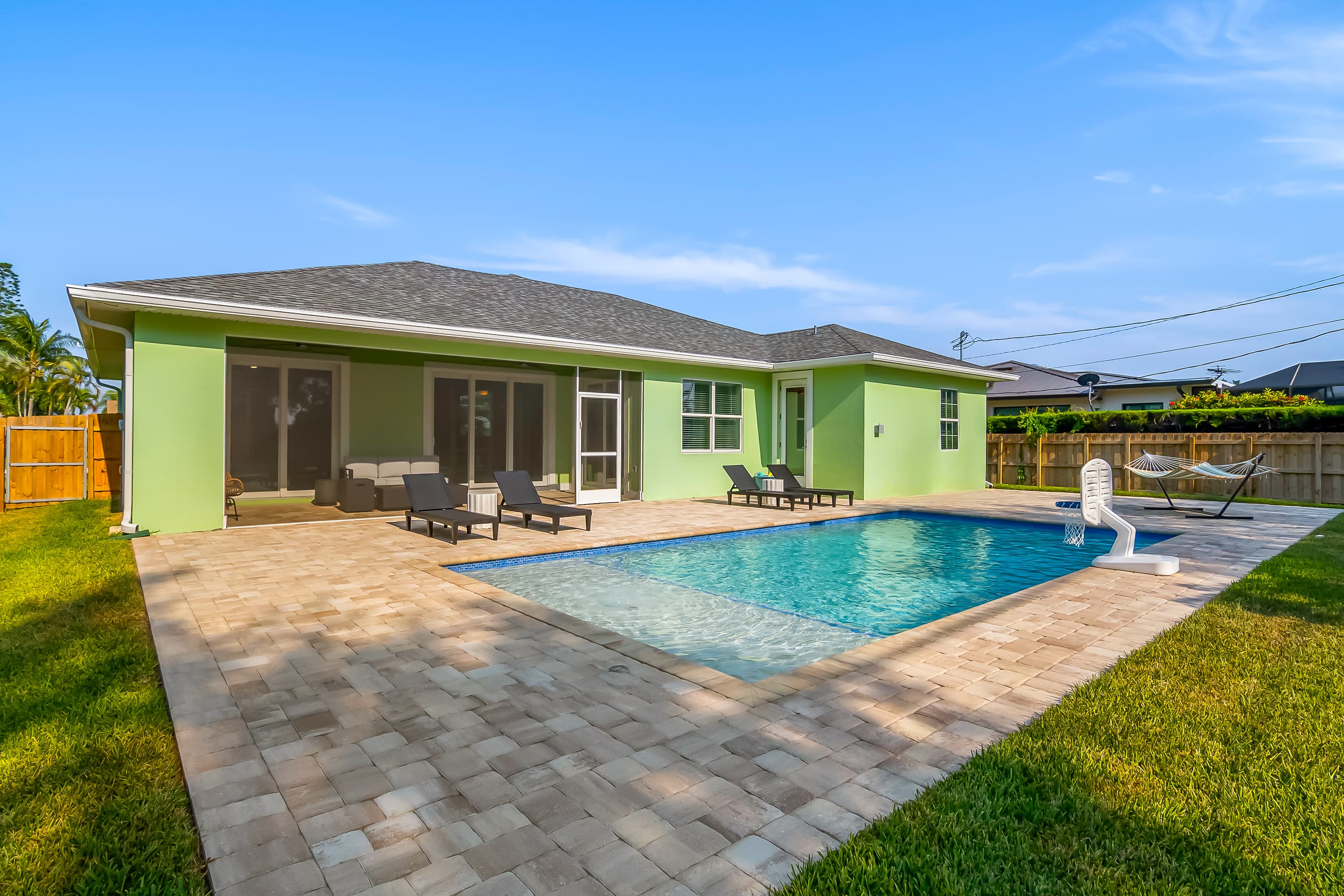 Swimming pool with stone paved deck, lounge chairs, green lawn, and light green house in background
