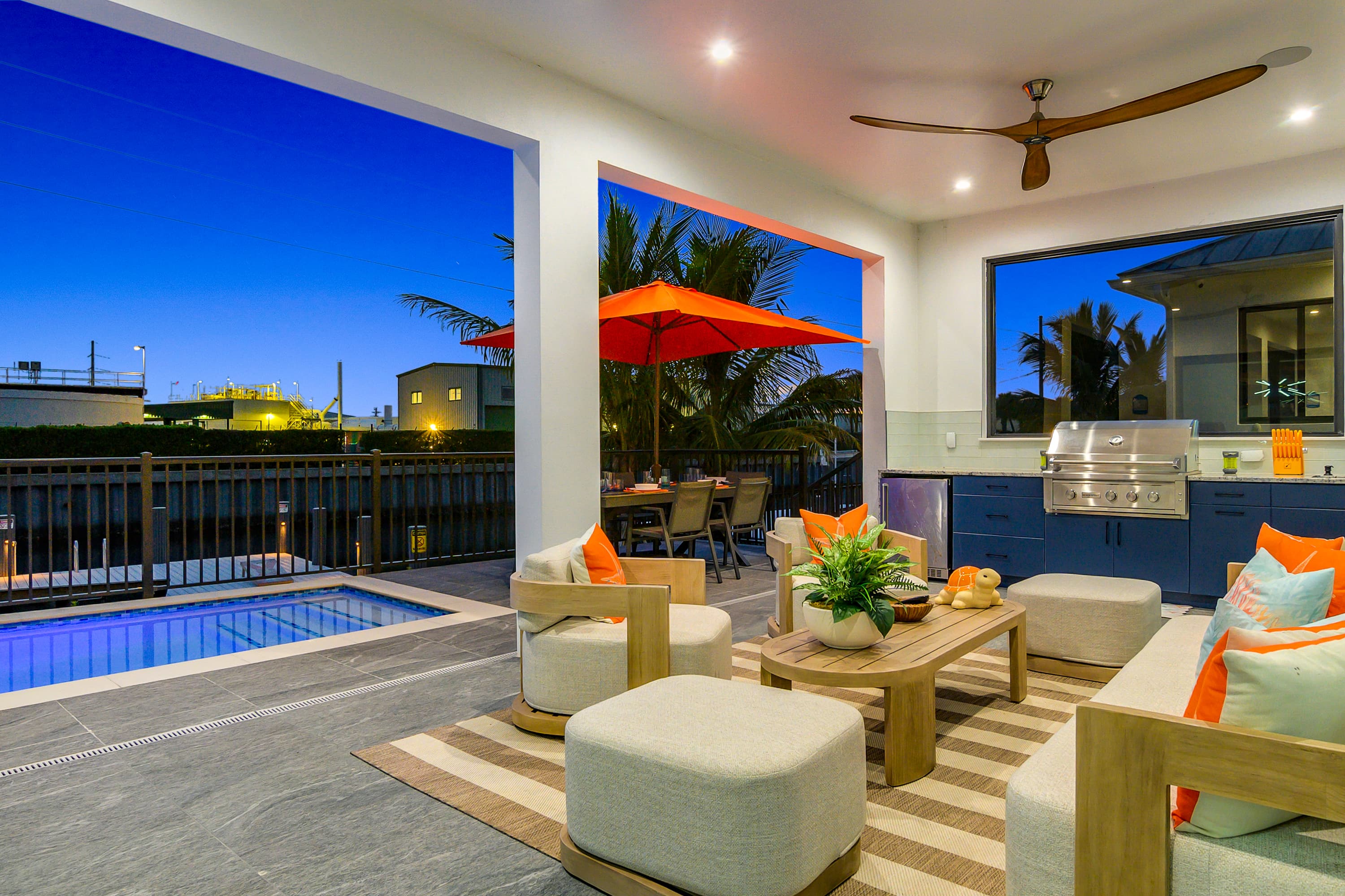 Covered outdoor lounge with sofa, chairs, a coffee table, ceiling fan, barbecue grill, and view of pool and waterfront at dusk