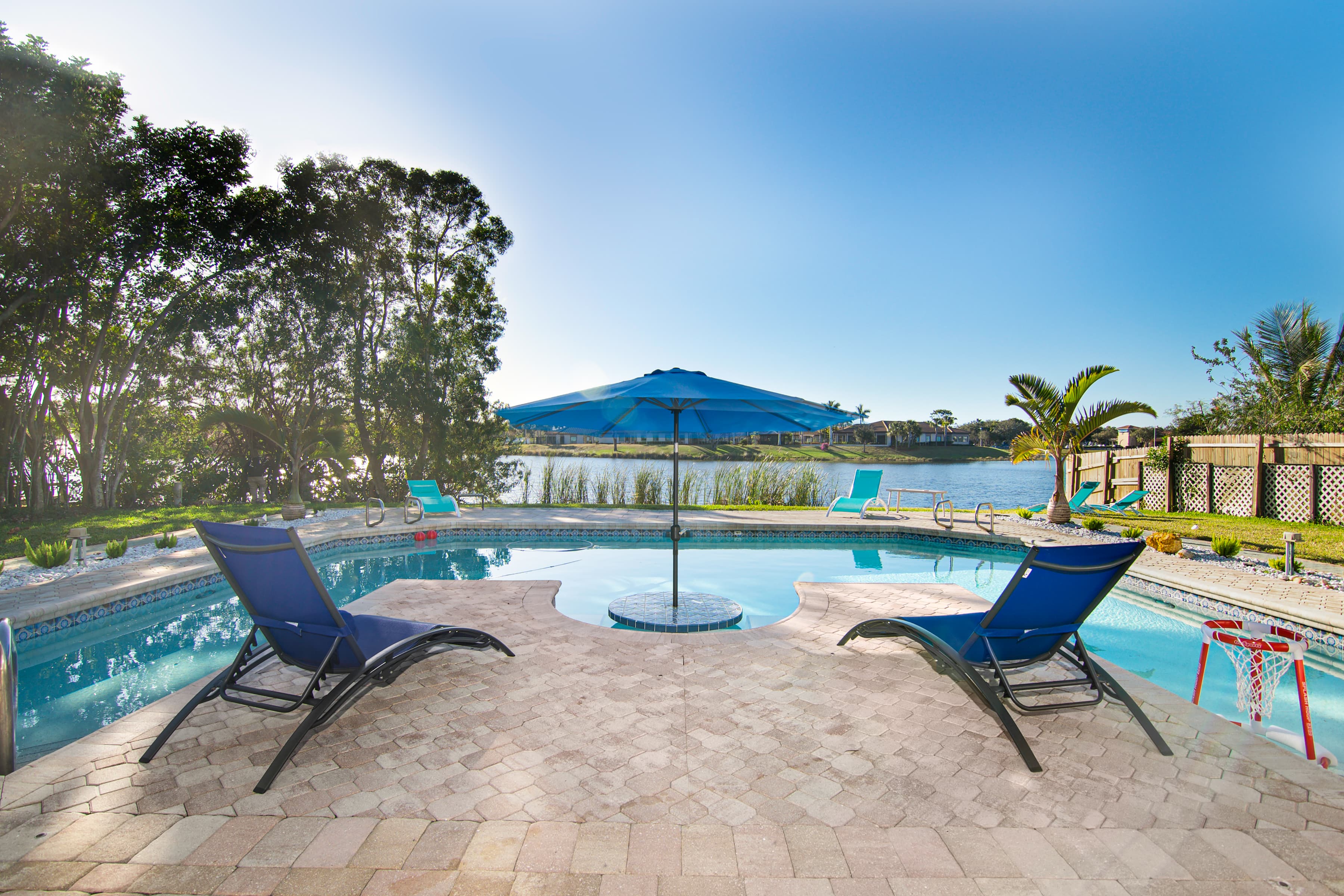 Swimming pool with lounge chairs and blue umbrella beside a lake under bright sky