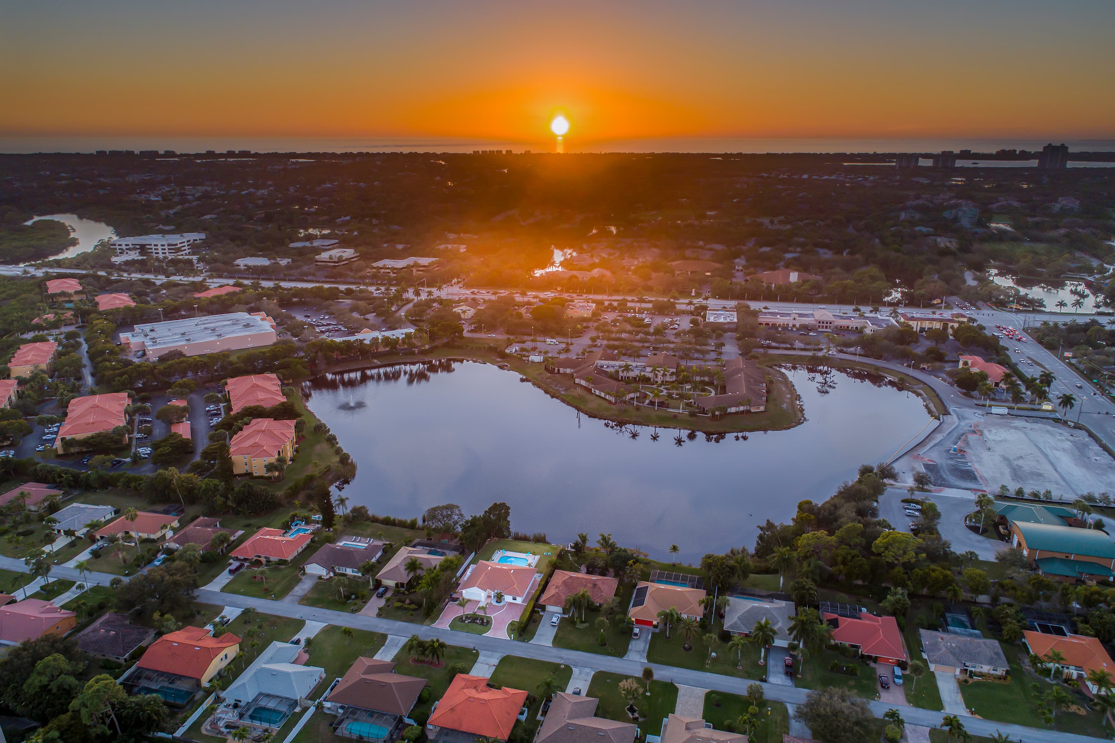 Aerial view of a lake and surrounding neighborhood under a colorful sunset sky